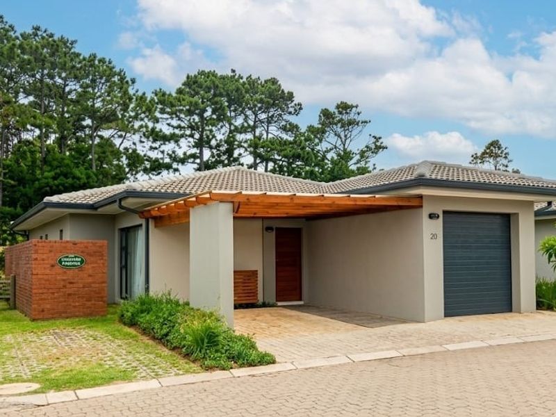 Front elevation of a modern townhouse featuring a paved driveway, integrated garage, timber pergola entrance, and well-maintained garden area.