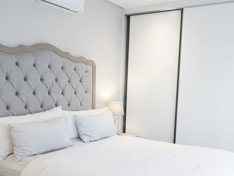 A well-maintained bedroom featuring a large built-in sliding door wardrobe and a wall-mounted air conditioning unit for climate control.