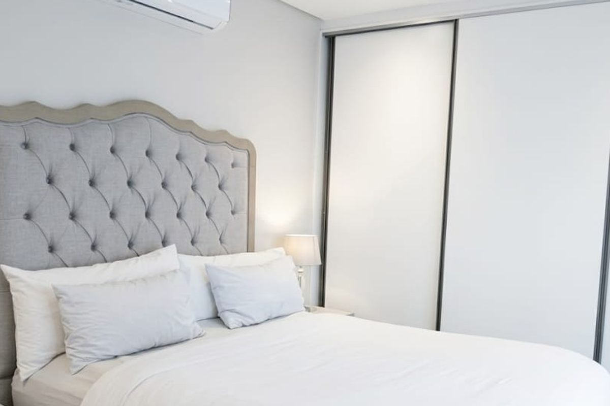 A well-maintained bedroom featuring a large built-in sliding door wardrobe and a wall-mounted air conditioning unit for climate control.