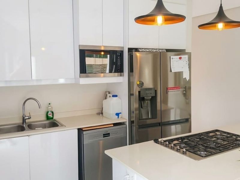 Modern kitchen featuring white cabinetry, stone countertops, a central island with a gas cooktop, and integrated stainless steel appliances.