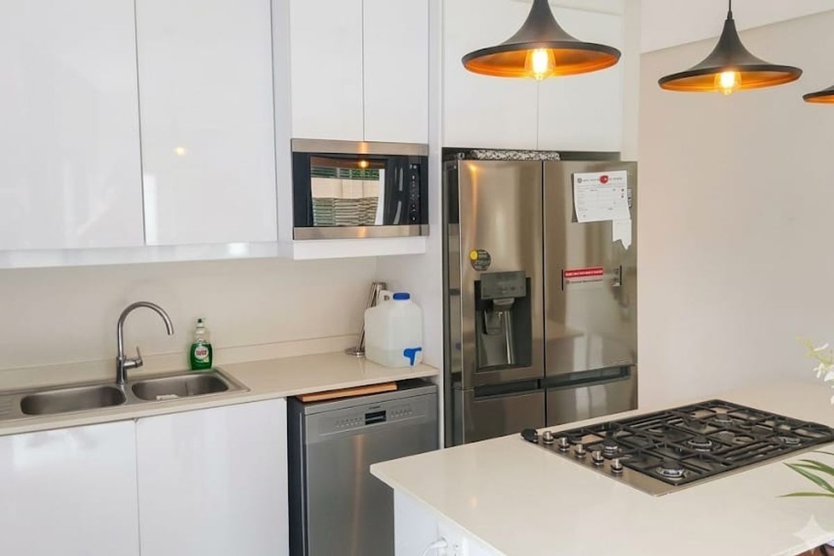 Modern kitchen featuring white cabinetry, stone countertops, a central island with a gas cooktop, and integrated stainless steel appliances.