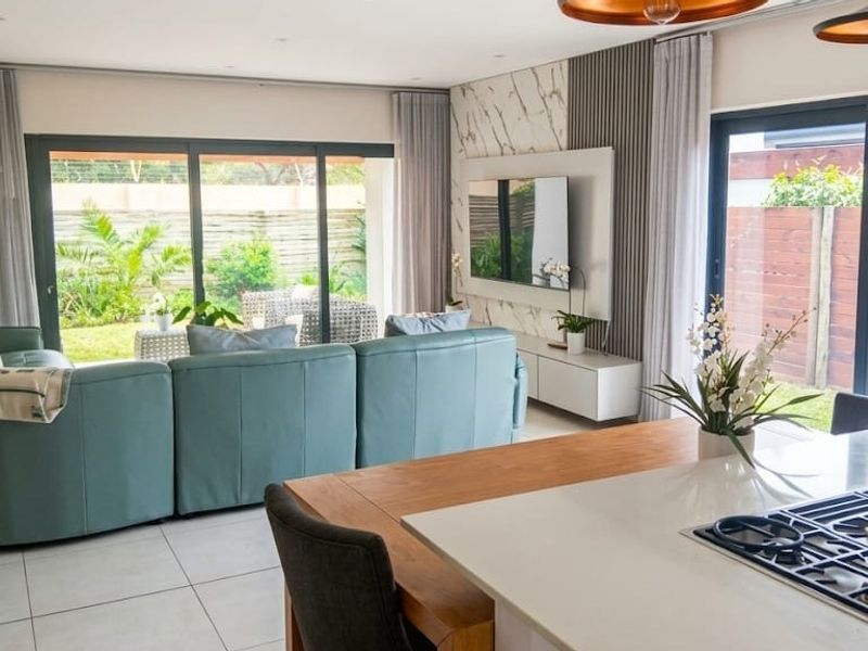 Modern open-plan living area featuring a sleek kitchen island with gas hob, large sliding doors to the garden, and contemporary feature wall paneling.