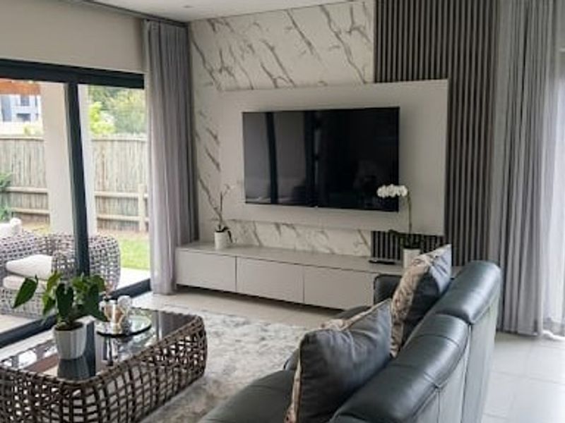 Modern living room featuring a marble-look feature wall, built-in media cabinetry, slatted timber accents, and large sliding doors opening to the garden.