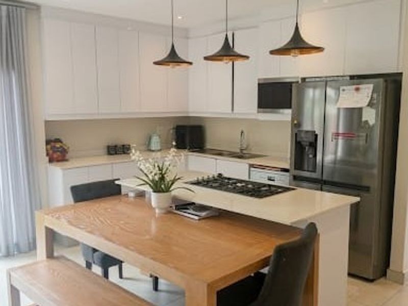 Modern open-plan kitchen featuring sleek white cabinetry, stone countertops, a gas cooktop, and integrated appliances, seamlessly flowing into the dining area with garden access.