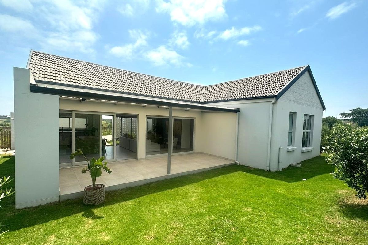 Rear view of the house featuring a covered patio with tiled flooring, sliding glass doors, and a well-maintained lawn.