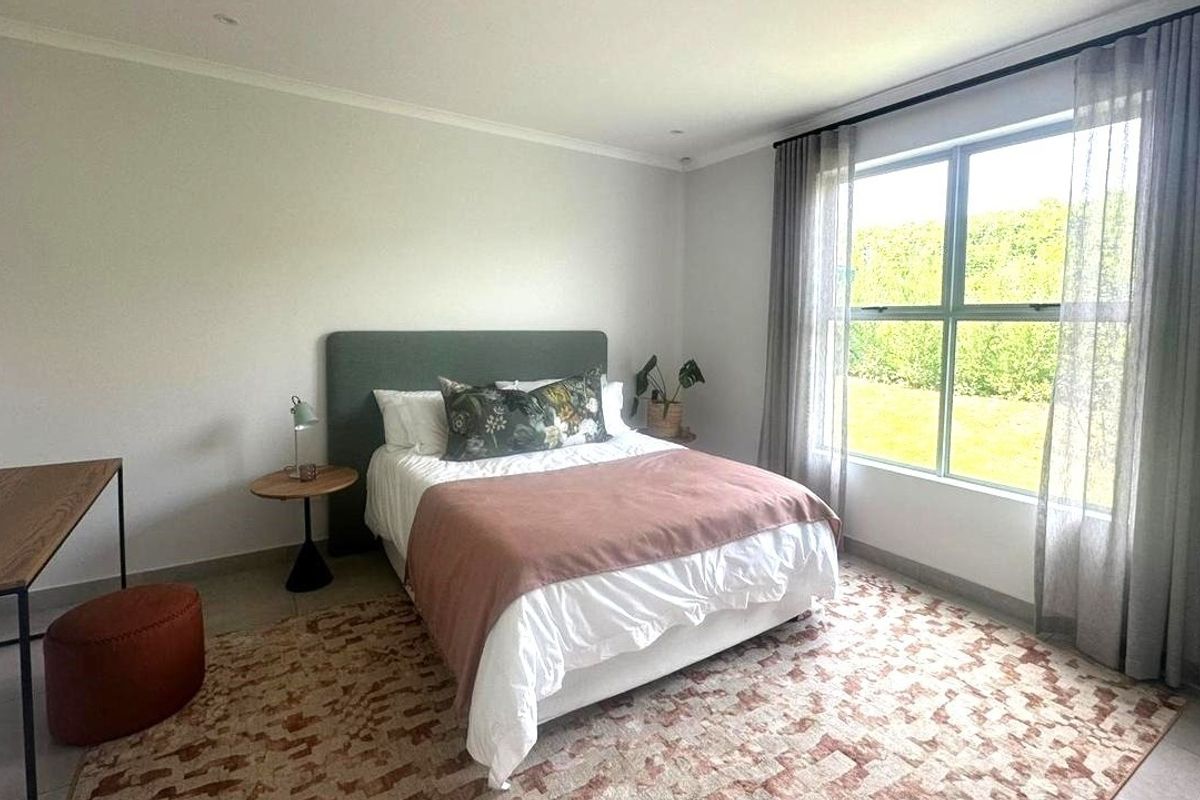 A bright and spacious bedroom featuring neutral walls, tiled flooring, and a large window that provides ample natural light.