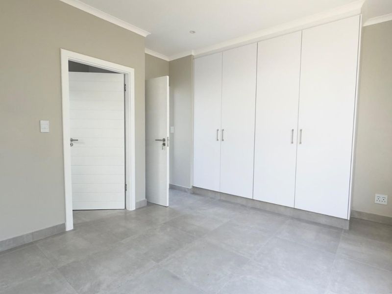 A clean, modern bedroom featuring neutral wall tones, large format floor tiles, and extensive built-in cupboard storage.