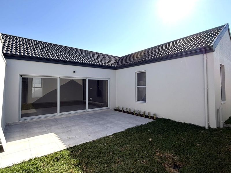 Rear view of the property featuring a paved patio area, sliding glass doors, and a well-maintained lawn.