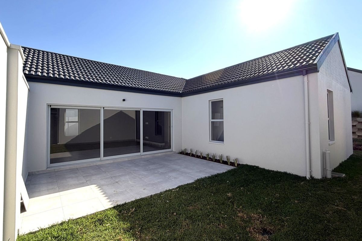 Rear view of the property featuring a paved patio area, sliding glass doors, and a well-maintained lawn.