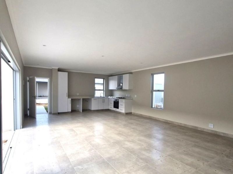 Spacious open-plan living area featuring a modern kitchen with built-in appliances, tiled flooring, and large sliding doors leading to the exterior.