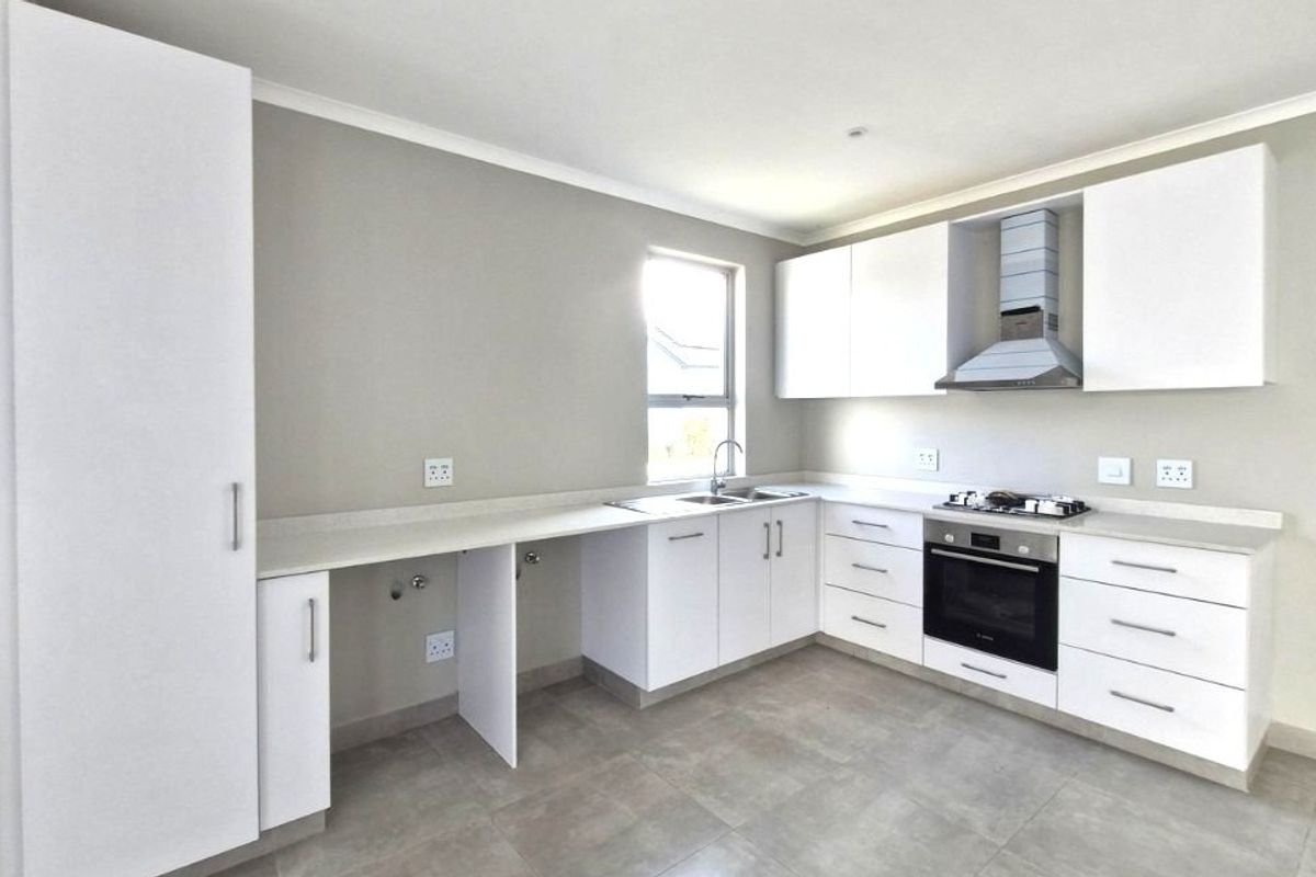 Modern, clean-lined kitchen featuring white cabinetry, stone countertops, integrated oven, gas hob, and extractor fan with neutral tiled flooring.
