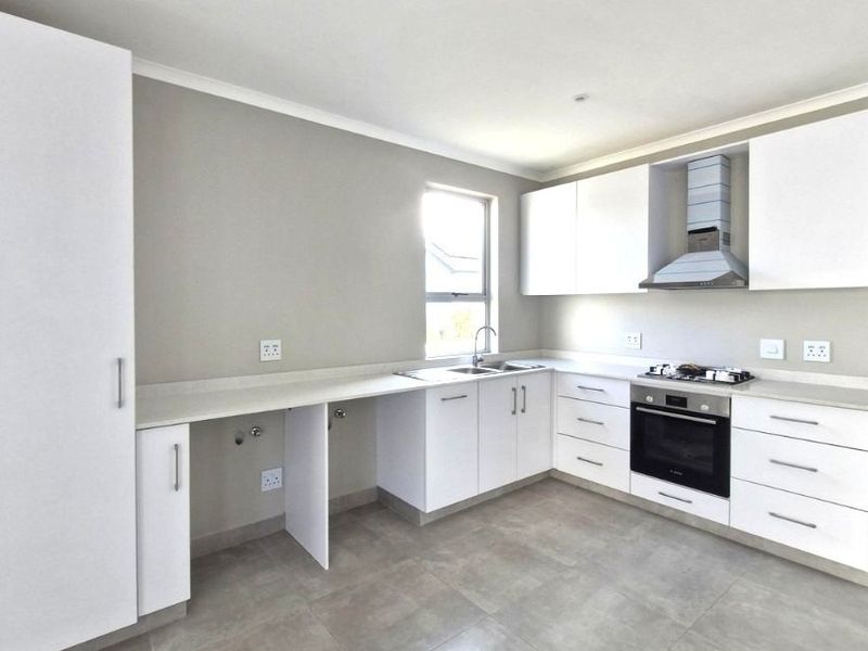Modern, clean-lined kitchen featuring white cabinetry, stone countertops, integrated oven, gas hob, and extractor fan with neutral tiled flooring.