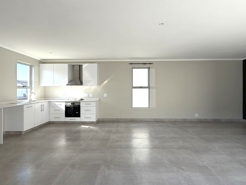 Spacious open-plan living area featuring a modern kitchen with built-in cabinetry, oven, hob, and extractor fan, finished with neutral walls and tiled flooring.