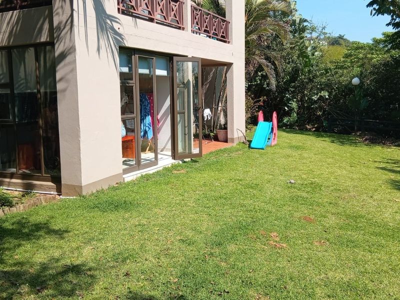 Rear view of the apartment featuring a private garden, lawn area, and access to the ground floor via aluminium sliding doors.