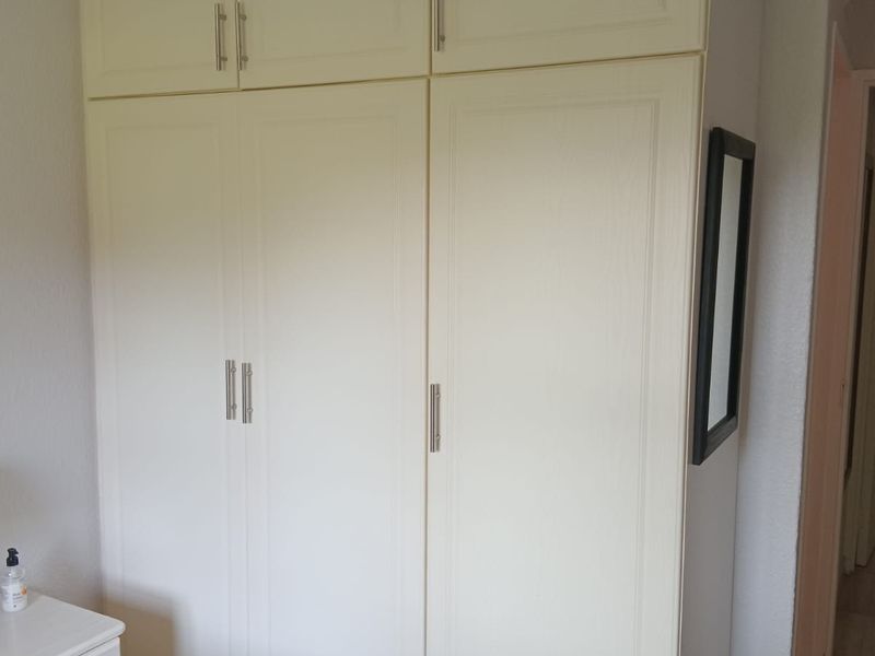 A bedroom featuring floor-to-ceiling built-in cupboards with modern handles, providing ample storage space.