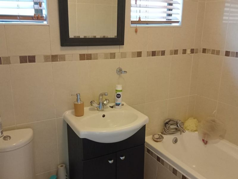 A functional bathroom featuring a vanity cabinet with basin, a standard toilet, and a bathtub with tiled walls and mosaic accents.