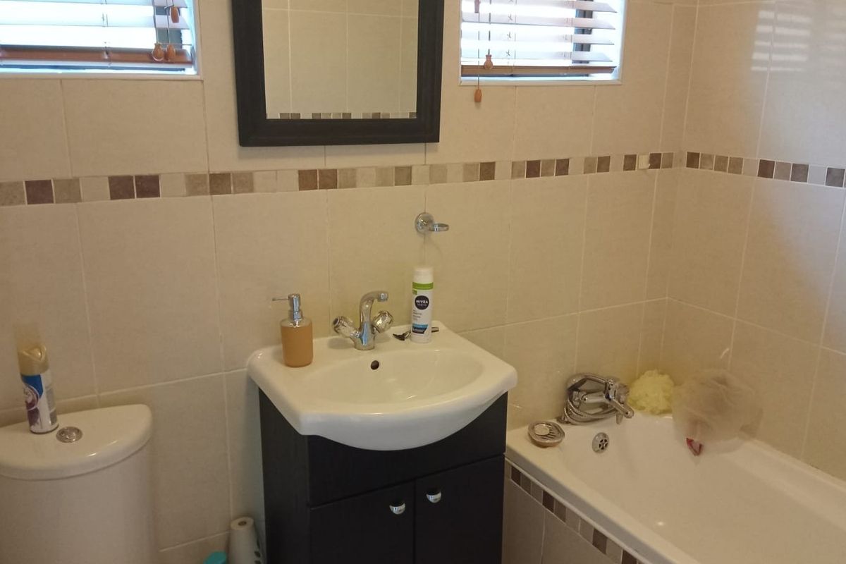 A functional bathroom featuring a vanity cabinet with basin, a standard toilet, and a bathtub with tiled walls and mosaic accents.