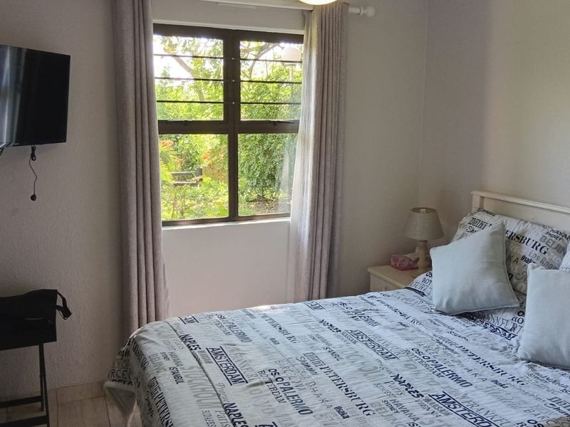 A functional bedroom featuring tiled flooring and a window with security bars, offering a view of the surrounding greenery.