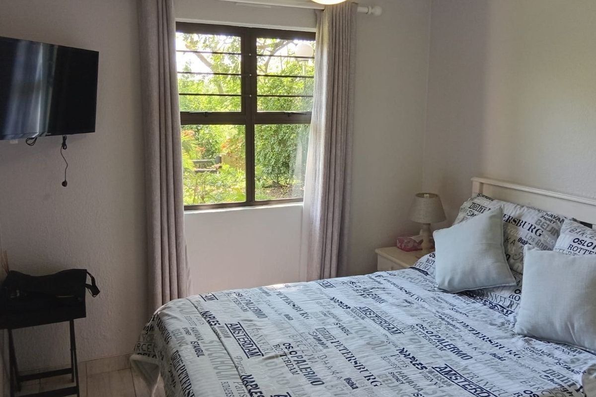 A functional bedroom featuring tiled flooring and a window with security bars, offering a view of the surrounding greenery.