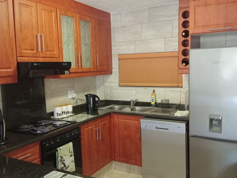A functional kitchen featuring warm-toned wooden cabinetry, granite countertops, a tiled backsplash, and integrated appliances including a hob, oven, and extractor fan.