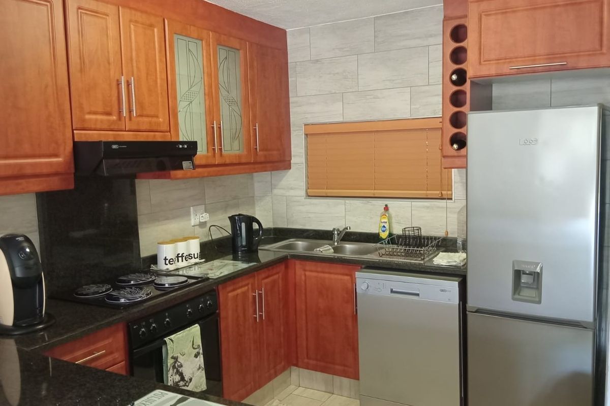 A functional kitchen featuring warm-toned wooden cabinetry, granite countertops, a tiled backsplash, and integrated appliances including a hob, oven, and extractor fan.