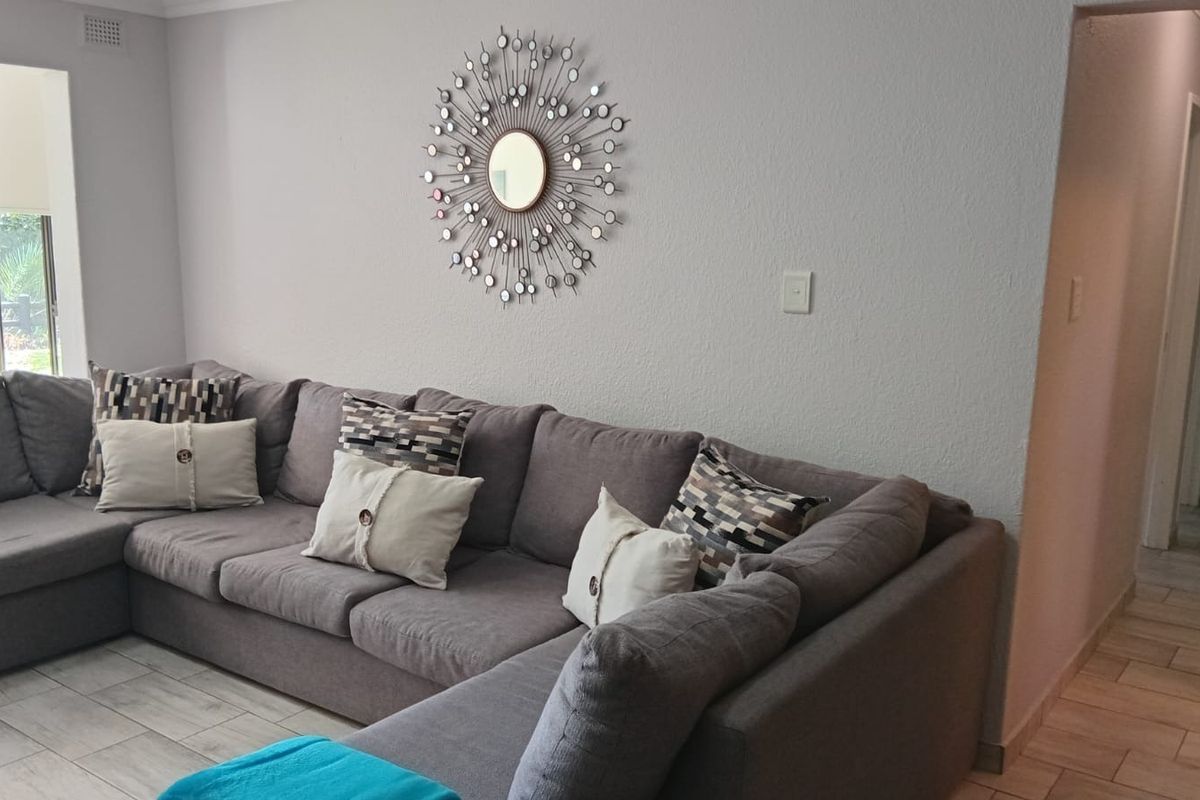 A well-maintained living room featuring neutral tiled flooring and a clean, minimalist aesthetic with access to an adjacent hallway.
