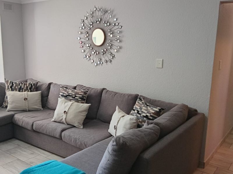 A well-maintained living room featuring neutral tiled flooring and a clean, minimalist aesthetic with access to an adjacent hallway.