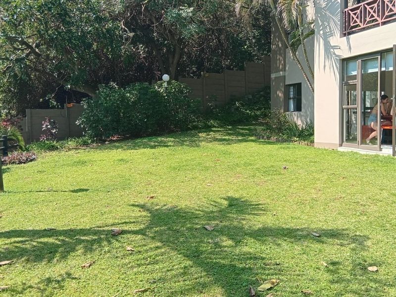 A well-maintained private garden area featuring a lush lawn, perimeter boundary wall, and direct access to the apartment interior via sliding glass doors.