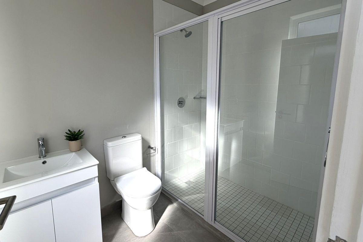 A clean, modern bathroom featuring a white vanity, toilet, and a glass-enclosed shower with tiled finishes.