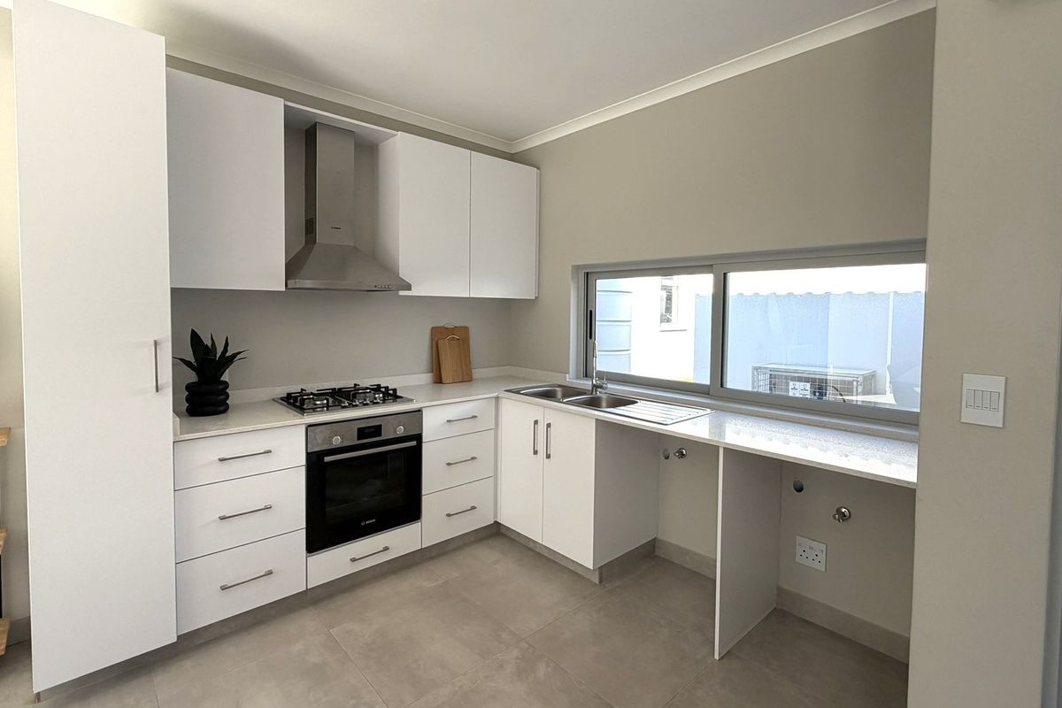Modern kitchen featuring white cabinetry, stone countertops, gas hob, electric oven, and stainless steel extractor fan with tiled flooring and natural light.