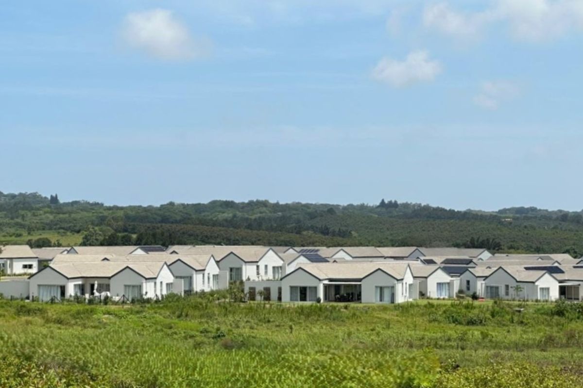 An aerial view of a modern residential estate featuring multiple detached homes with tiled roofs and integrated solar panels set in a landscaped environment.