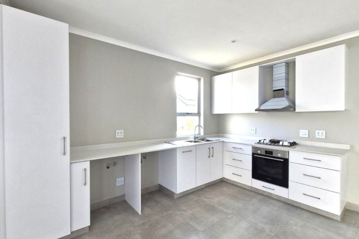 Modern, clean-lined kitchen featuring white cabinetry, stone countertops, integrated oven, gas hob, and extractor fan, finished with neutral tiled flooring.