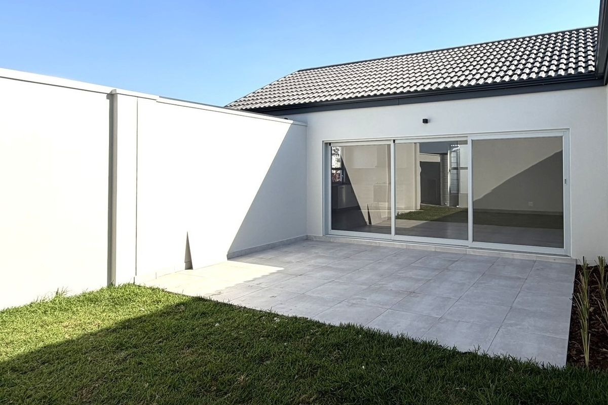 A clean, modern rear exterior featuring a paved patio area, manicured lawn, and large sliding glass doors leading into the home.