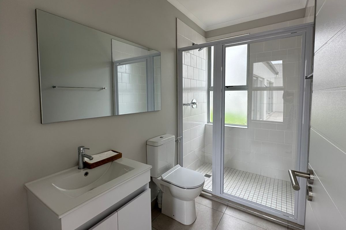 A clean, modern bathroom featuring a vanity with basin, toilet, and a glass-enclosed shower with tiled finishes.