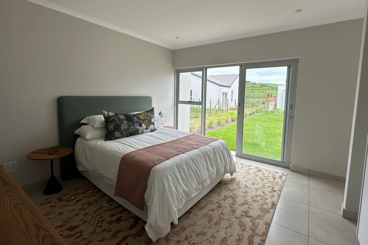Modern bedroom featuring neutral walls, tiled flooring, recessed lighting, and a large sliding glass door providing direct access to the garden.