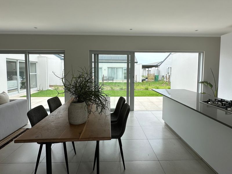 Modern open-plan living and dining area featuring a sleek kitchen with stone island, gas hob, and large sliding doors opening to the rear garden.