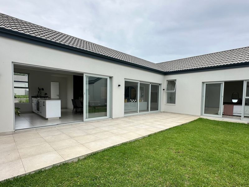 A modern rear exterior view featuring a spacious tiled patio, well-maintained lawn, and large sliding glass doors providing seamless indoor-outdoor flow.