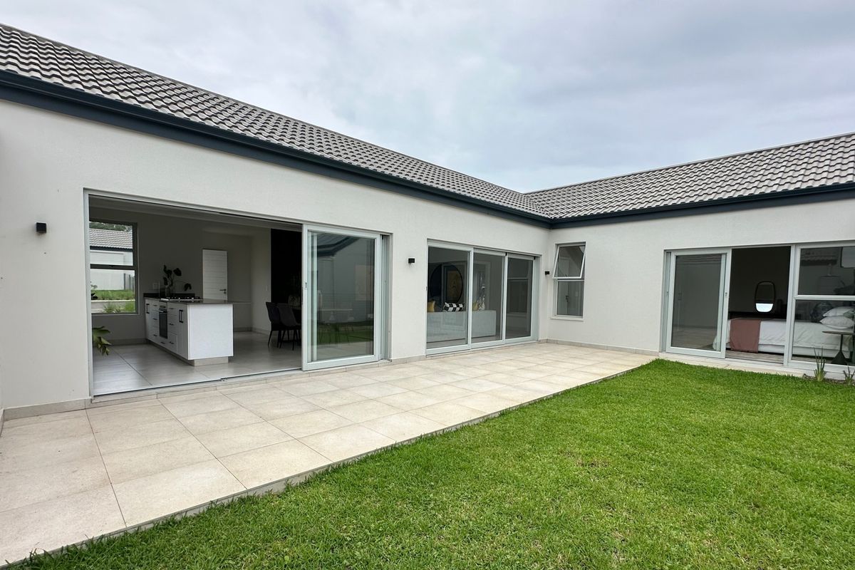 A modern rear exterior view featuring a spacious tiled patio, well-maintained lawn, and large sliding glass doors providing seamless indoor-outdoor flow.