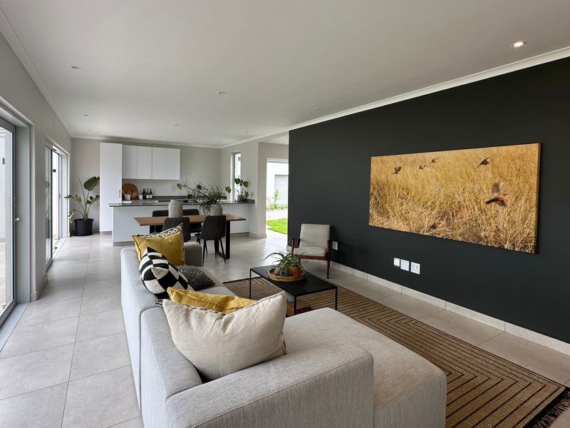 Modern open-plan living area featuring tiled floors, recessed lighting, and seamless flow to the kitchen and outdoor patio through large sliding glass doors.
