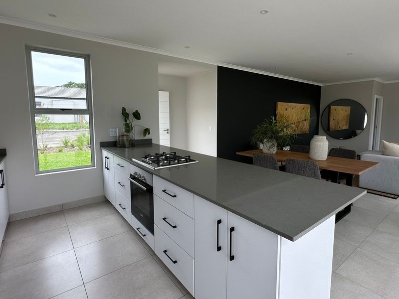 Modern open-plan kitchen and living area featuring a central island with gas hob, stone countertops, and sleek white cabinetry with contemporary finishes.