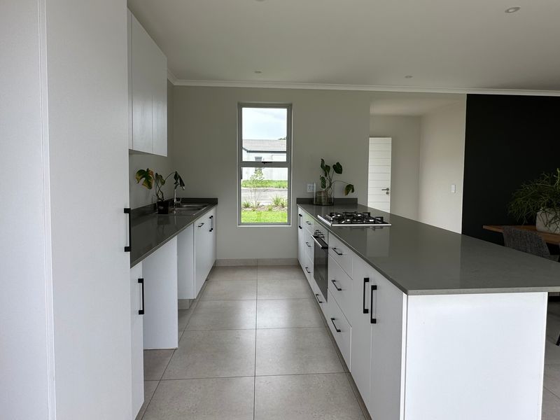 Modern kitchen featuring white cabinetry, stone countertops, a central island with a gas hob, built-in oven, and tiled flooring.