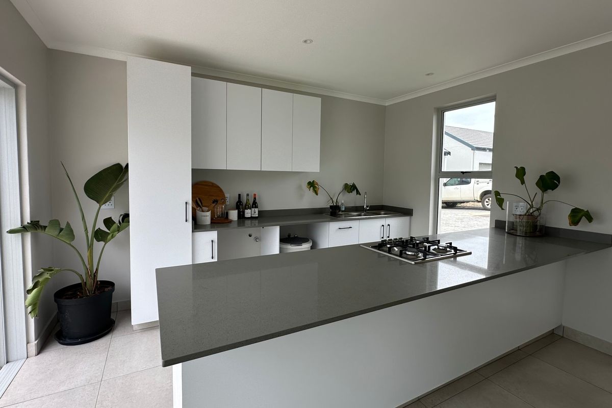 Modern kitchen featuring white cabinetry, stone countertops, a central island with a gas hob, and direct access to an outdoor patio area.
