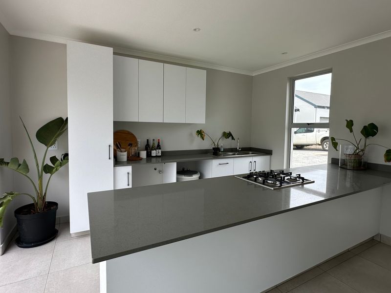 Modern kitchen featuring white cabinetry, stone countertops, a central island with a gas hob, and direct access to an outdoor patio area.