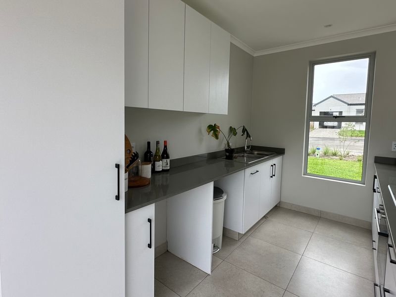 Modern scullery featuring sleek white cabinetry, dark stone countertops, stainless steel sink, and a built-in gas hob with large window for natural light.