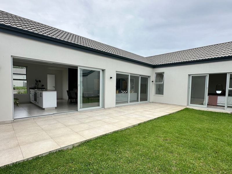A modern rear exterior view featuring a spacious tiled patio, well-maintained lawn, and large sliding glass doors providing seamless indoor-outdoor flow.