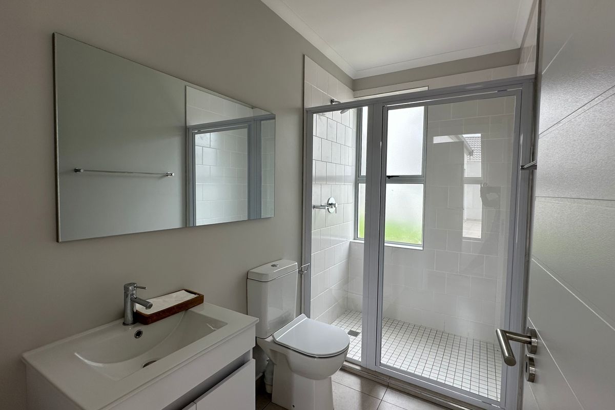 A clean, modern bathroom featuring a vanity with basin, a toilet, and a glass-enclosed shower with tiled finishes.