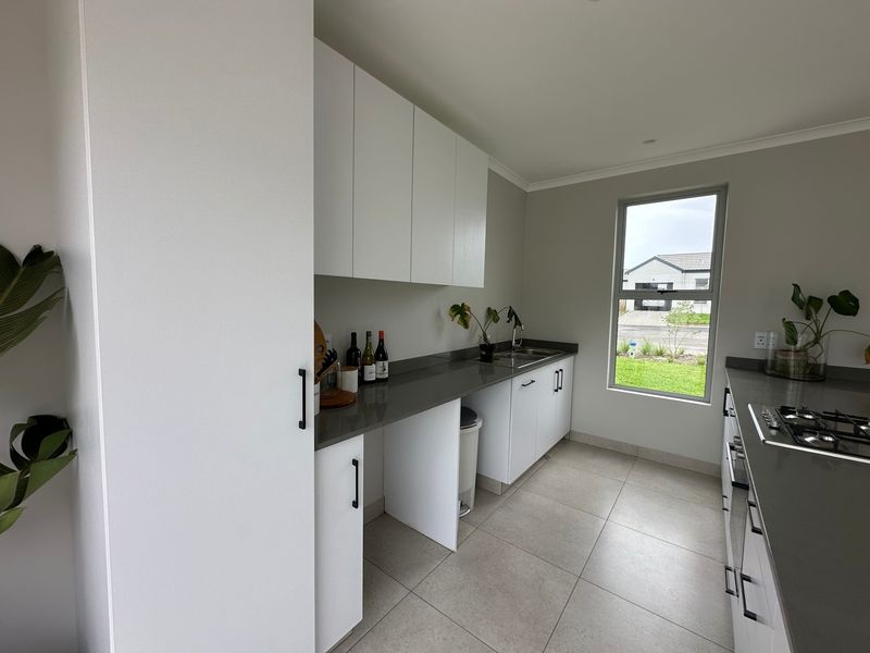 Modern scullery featuring sleek white cabinetry, dark stone countertops, stainless steel sink, and gas hob, with tiled flooring and a window overlooking the exterior.