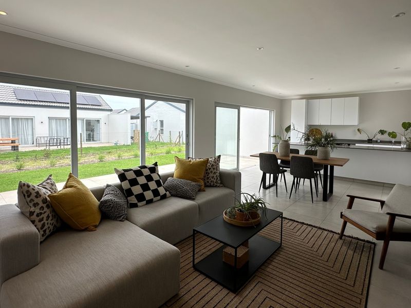 Modern open-plan living and dining area featuring large sliding glass doors, recessed lighting, and a sleek kitchen with island, opening onto a private garden.