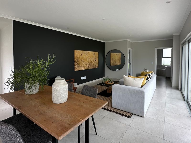 Modern open-plan living and dining area featuring large sliding glass doors, neutral tiled flooring, and a striking black accent wall.