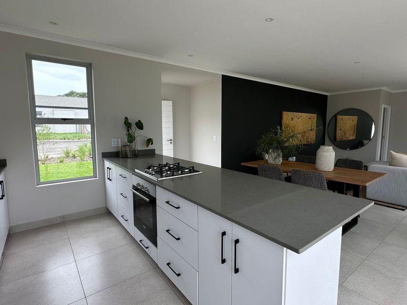 Modern open-plan kitchen and living area featuring a central island with gas hob, built-in oven, quartz countertops, and neutral tiled flooring.